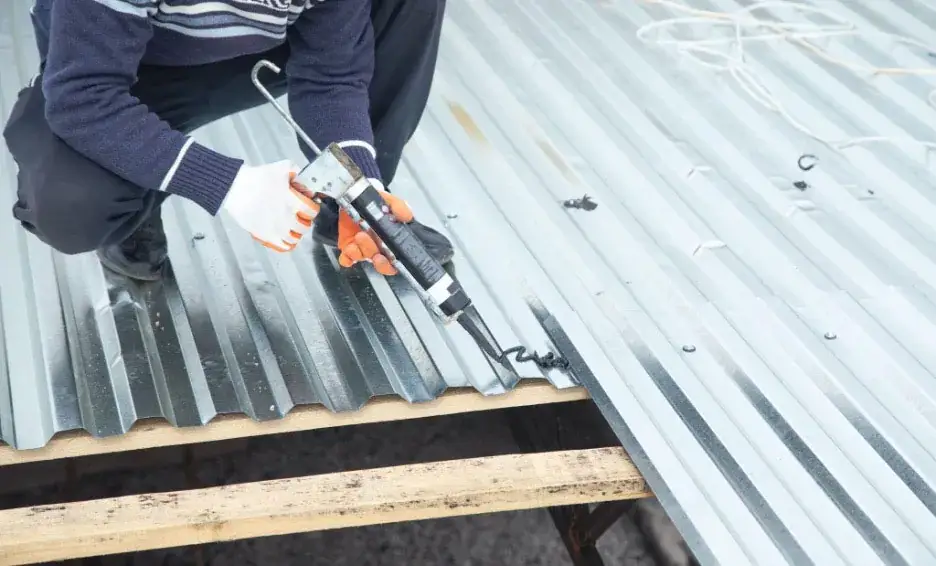 Sheet metal contractor applying adhesive to metal roof panels.